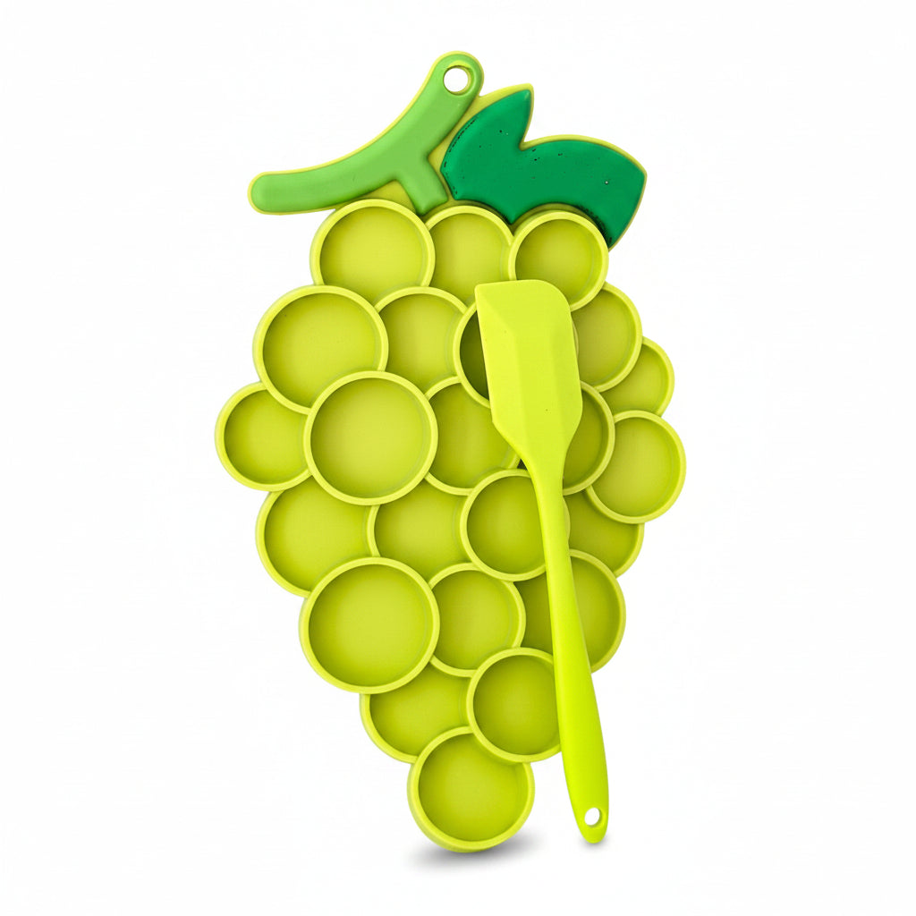 Green silicone ice cube tray shaped like a bunch of grapes with a spoon on a white surface.